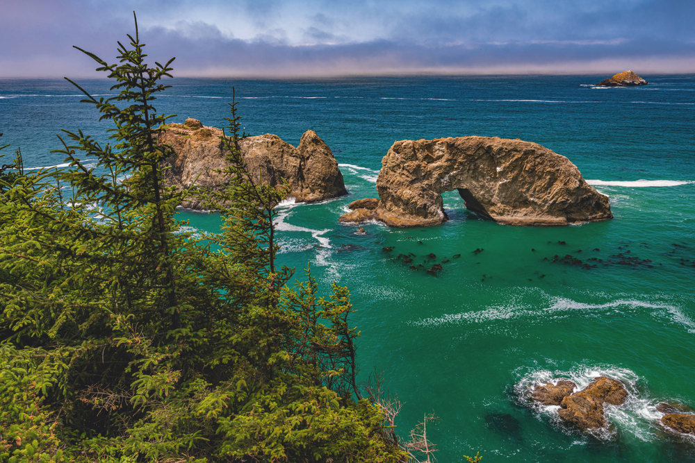 View looking down at Arch Rock in the beautifully colored ocean at sunset.