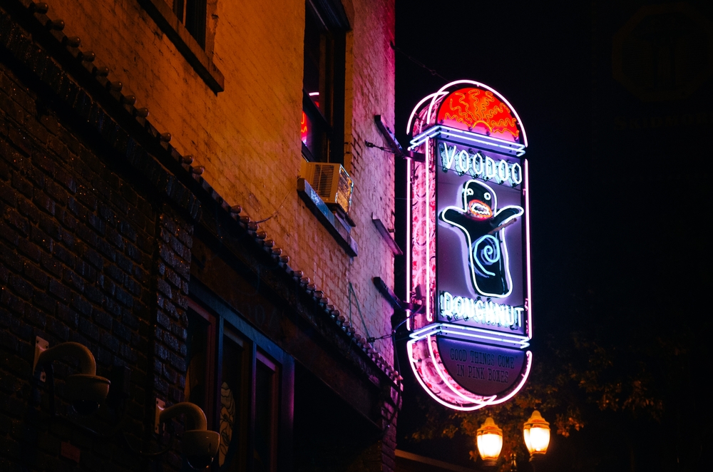 Nighttime at Voodoo Doughnut with a neon sign with a strange figure.