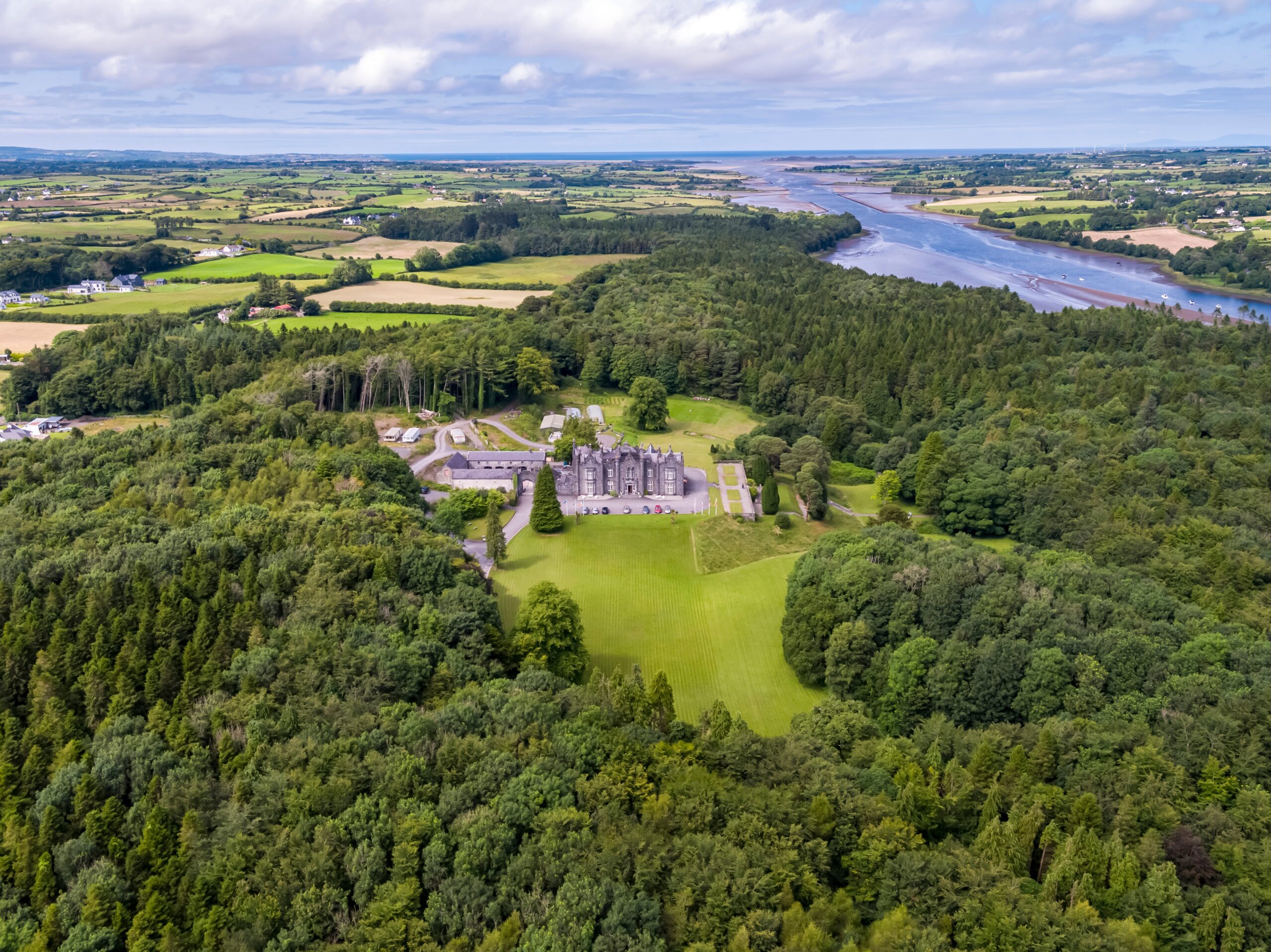 Aerial view of Belleek which shows this grey stone castle is surrounded by woodland and near a beautiful lake. 