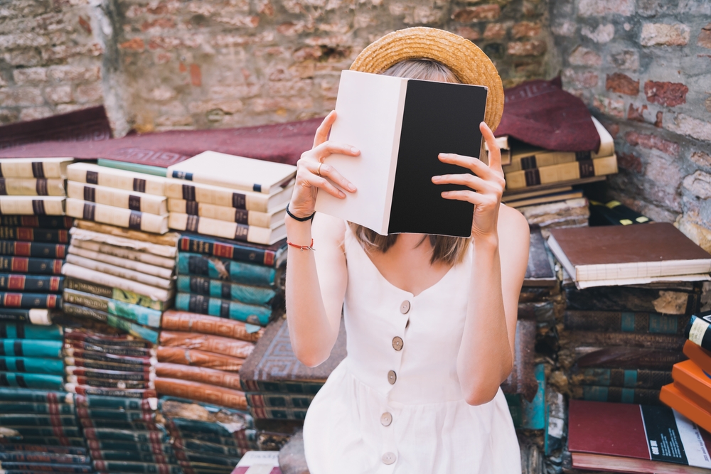 a girl in white dress in the second section of the bookstore Libreria Acqua Alta with a book covering herface