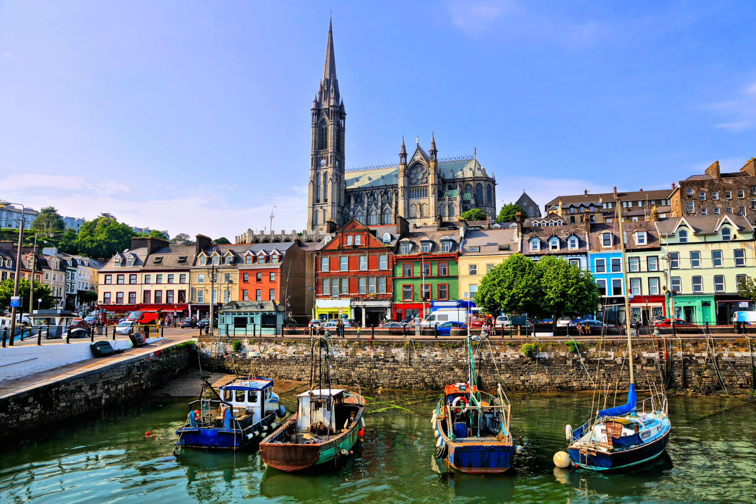 Beautiful view from the harbor of Cobh Ireland. The boats and businesses in the foreground are brightly colored and an epic gothic style cathedral is up a hill in the background.