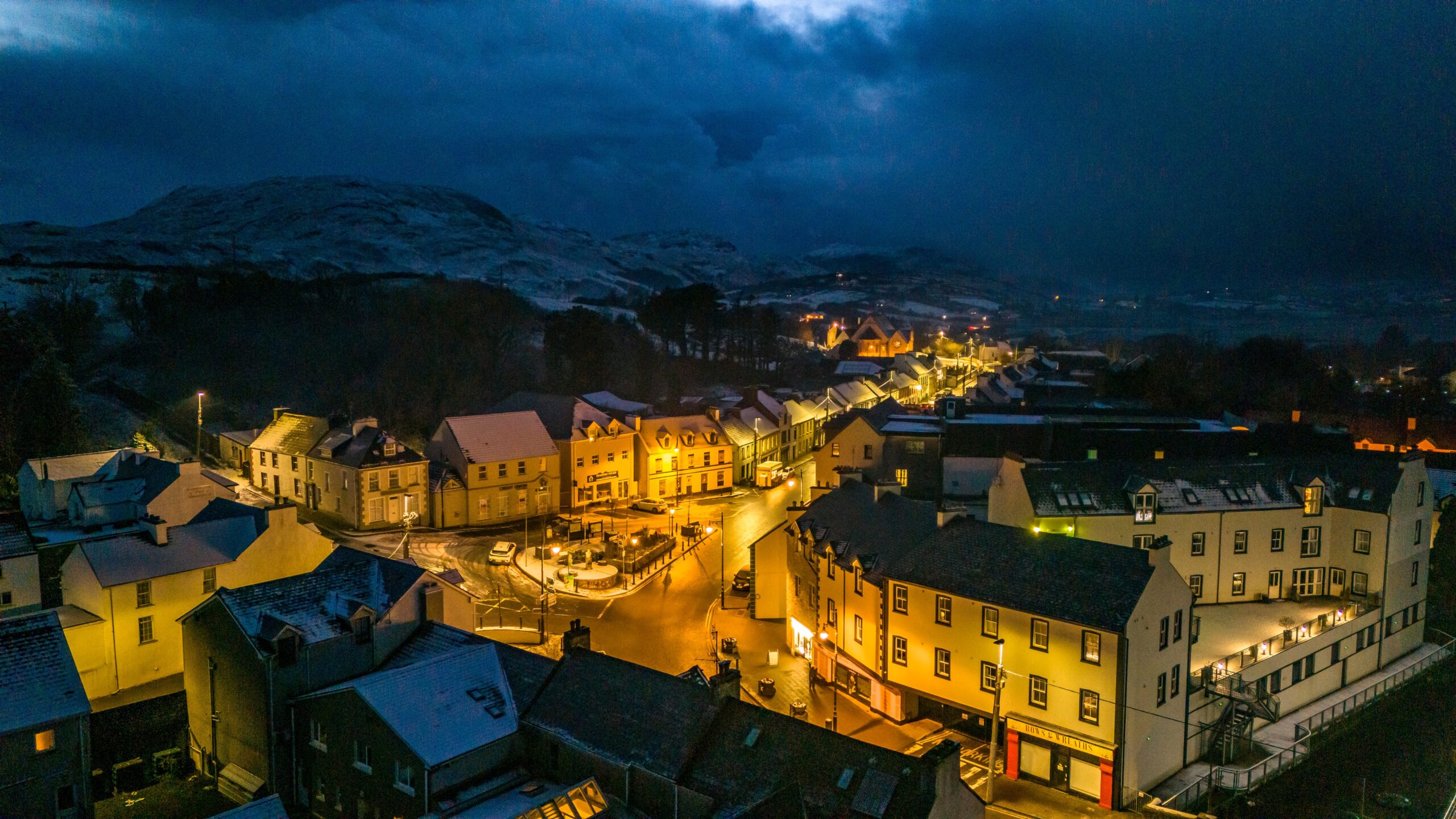 View of snow covered hills surrounding the brightly lit cozy downtown of Ardara, one of the cutest towns in Ireland. 
