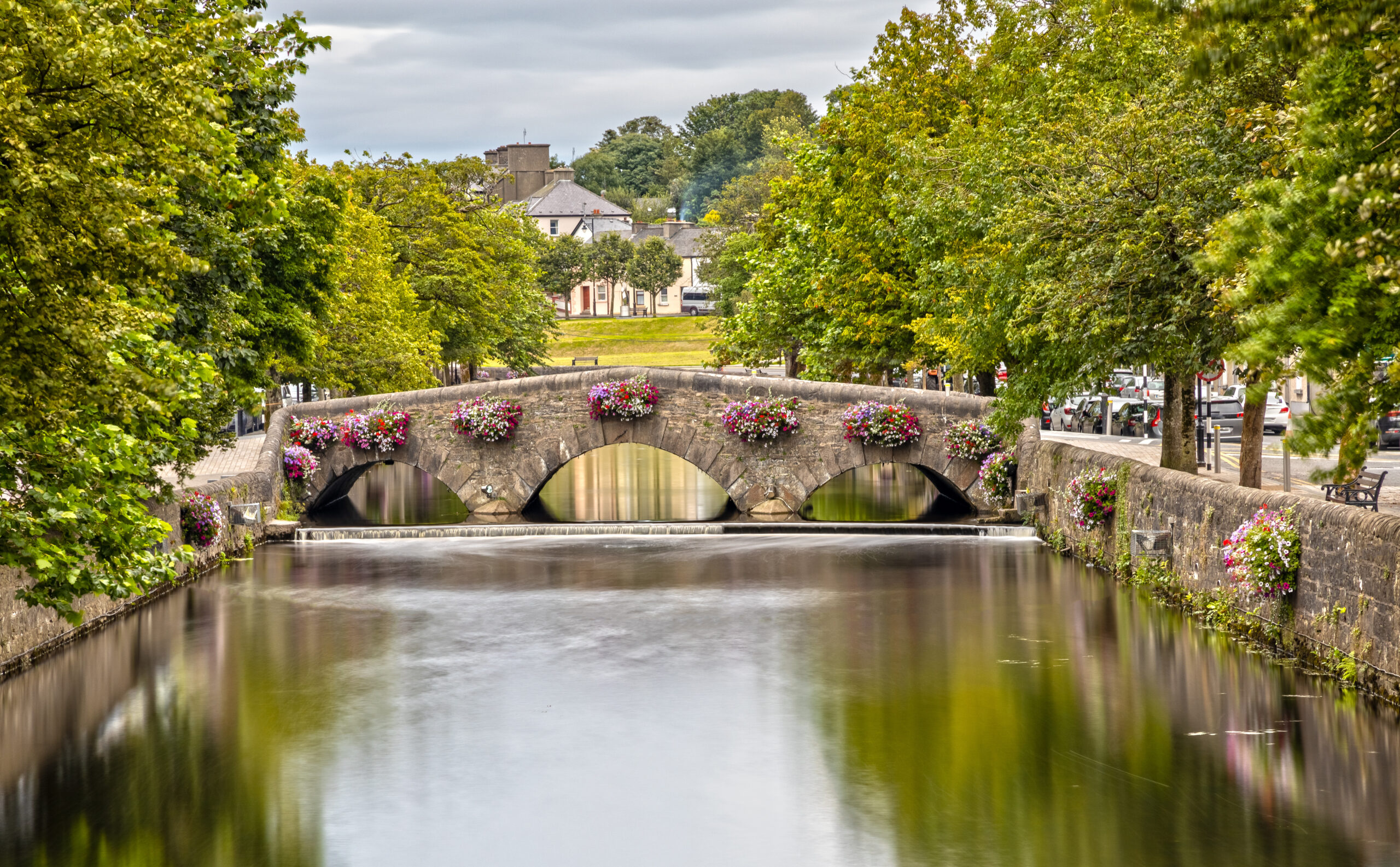 View of an adorable stone bridge decorated with flowers on a tree lined stream in Westport Ireland