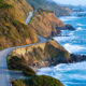 Aerial view of the Pacific Coast Highway in California along a rugged coastline with crashing waves during a West Coast road trip.
