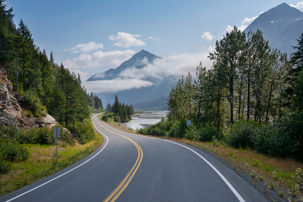 Highway cutting through the wilderness of Alaska with could covered mountains in the distance on a West Coast road trip.