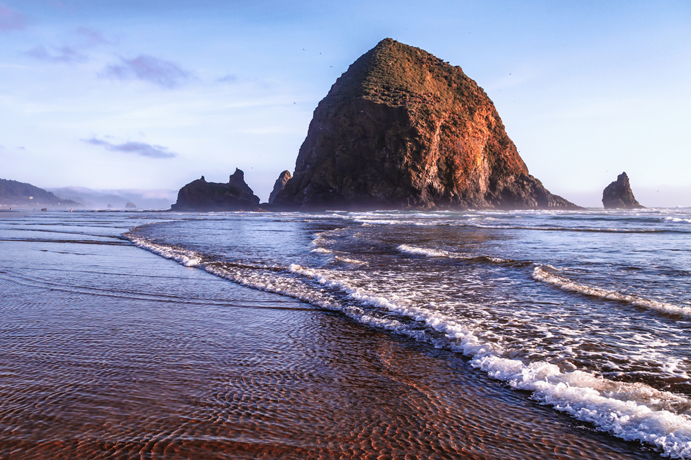 The famous Haystack Rock at Cannon Beach with waves rolling up on the sandy beach.
