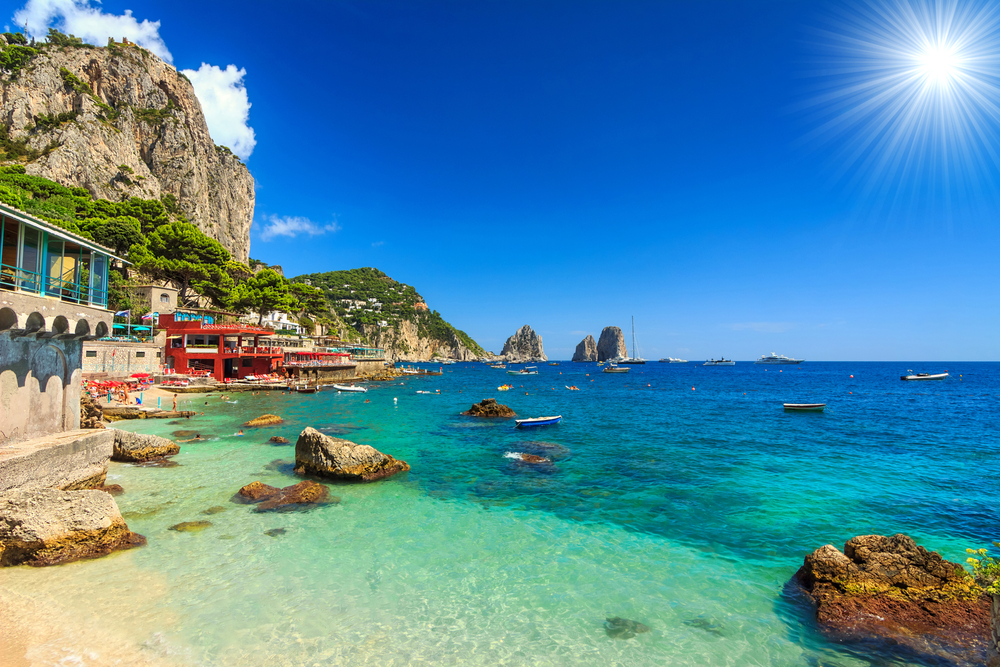 the beach club of Bangi Di Tiberrrio is one of the beach clubs in Capri with rocks on coat line and red beach club seen in background