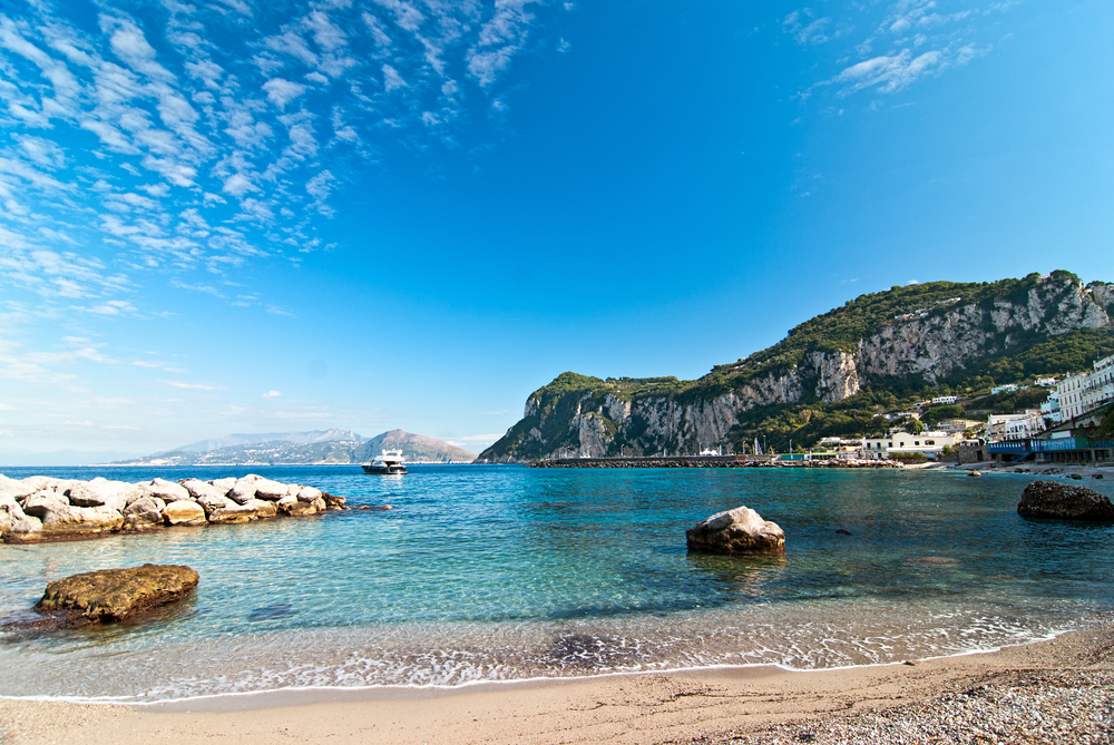 The calm sandy beach on the island of Capri with turquoise water and cliffs