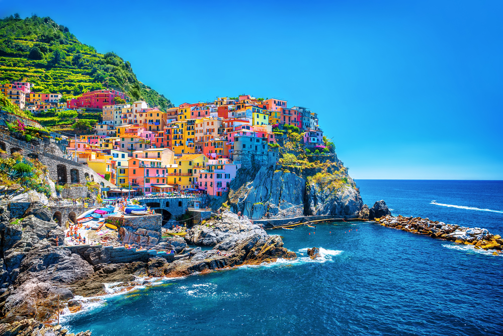 View of the colorful Italian architecture from the water at Cinque Terre. The ocean and sky are a beautiful blue. 