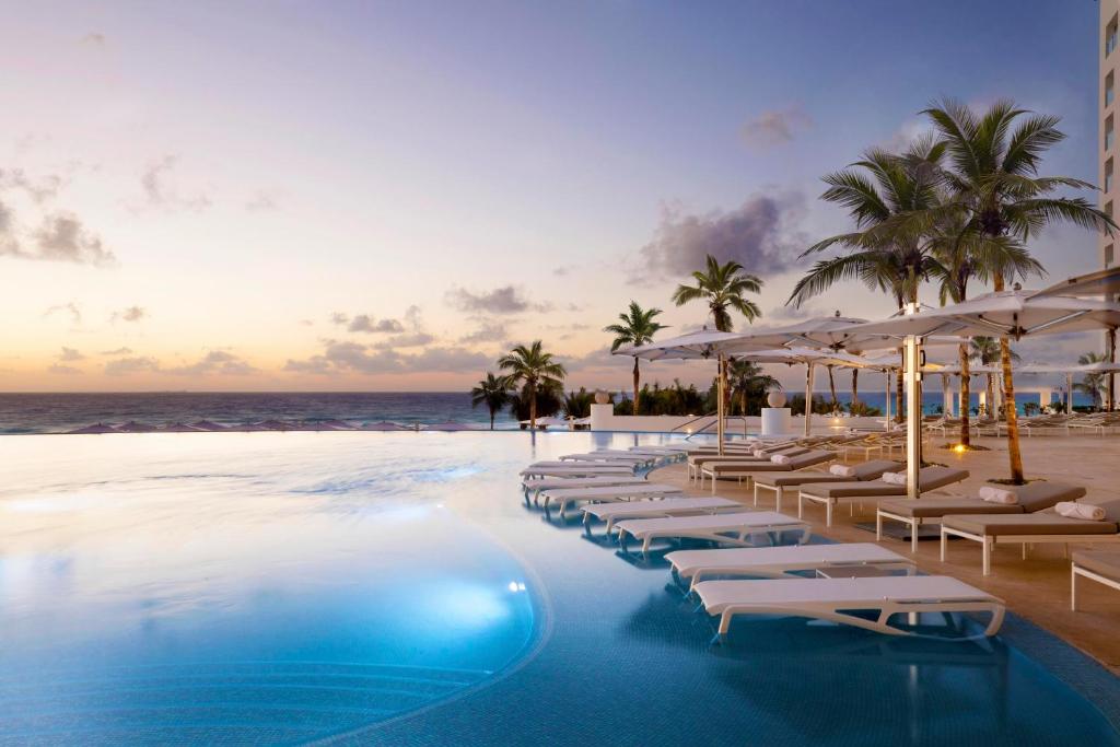 A wonderful hotel pool surrounded by palm trees and loungers with the sea in the distance. 