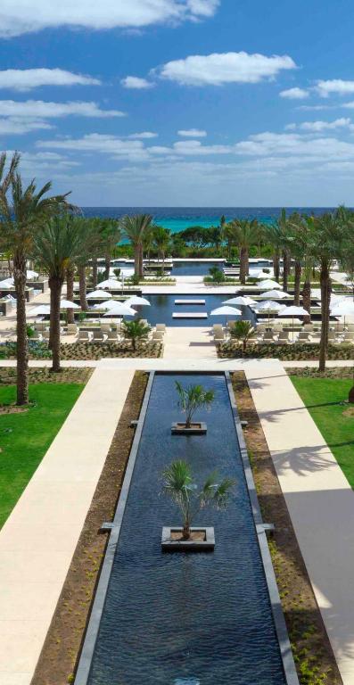 View of a long pool with a two swimming pools in the distance. It is surrounded by palm trees. 