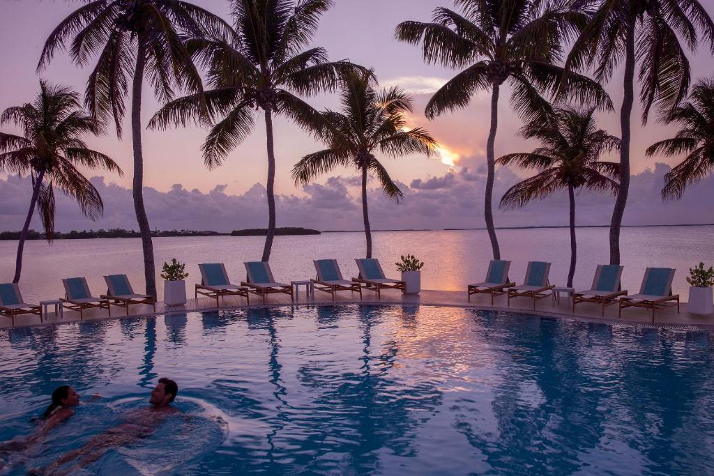 Couple swimming in a pool at sunset with the ocean in the background. The article is about the best adults only all inclusive resorts. 