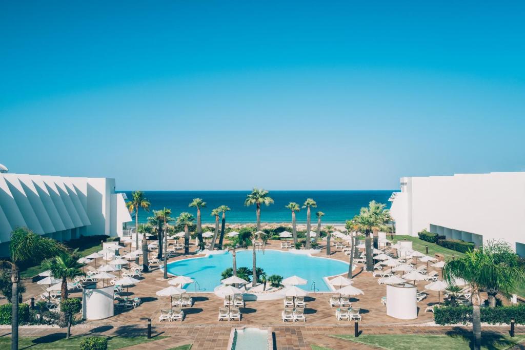 Picture of a hotel pool surround by chairs and trees with buildings at each side. 