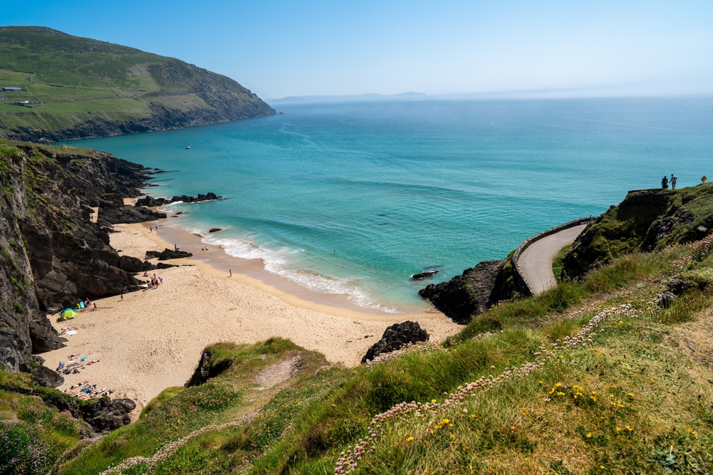 View of Coumeenoole Beach from a surrounding cliff. The sand is light in color and the ocean is a beautiful blue.