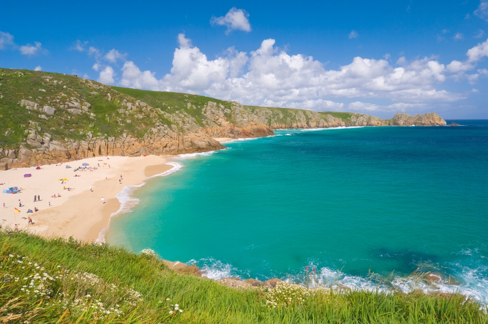 Porthcurno Beach in Cornwall has a light sand beach with crystal clear turquoise water surrounded by cliffs. 