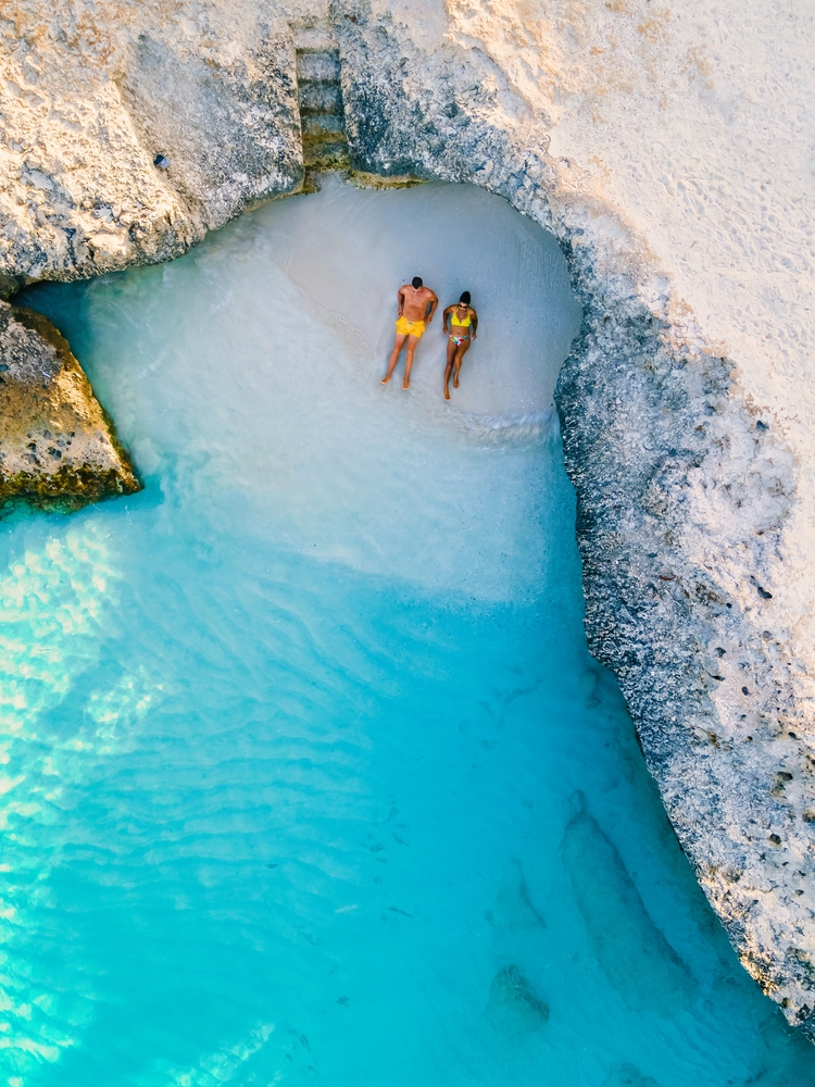 Man and woman relax on the very small beach of Tres Trapi Steps Beach Aruba, one of the best beaches in the Caribbean. 