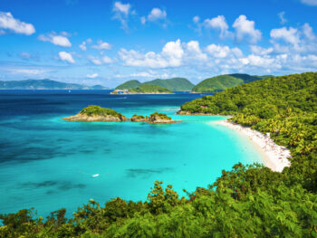 View looking down to Trunk Bay with the green trees on the right, a white sand beach, and vibrant blue water.