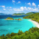 View looking down to Trunk Bay with the green trees on the right, a white sand beach, and vibrant blue water.