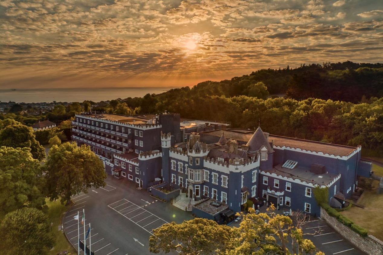 View of Fitzpatrick Castle's blue and white exterior with the sun rising over Dublin Bay in the distance. 