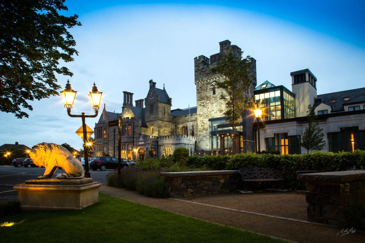 View of the epic stone and glass exterior of Clontarf Castle Hotel at twilight. This castle hotel in Dublin effortlessly blends the modern and historic in its exterior. 