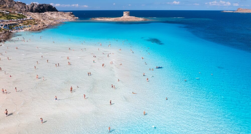 la pelosa beach in europe with clear blue water and people enjoying the beach. the sky is blue