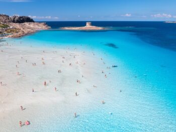 la pelosa beach in europe with clear blue water and people enjoying the beach. the sky is blue