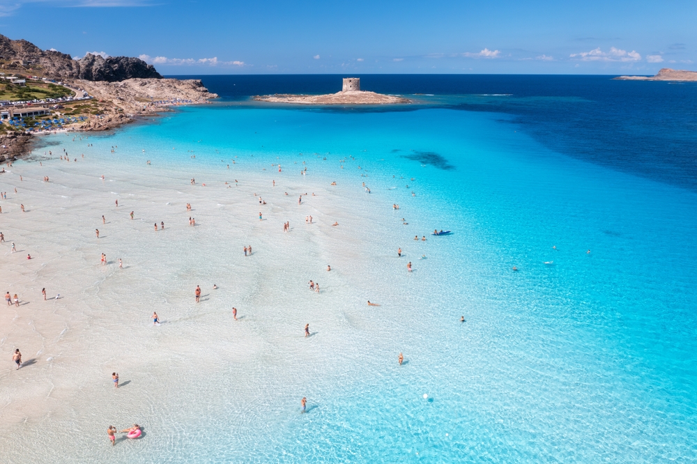 a large shallow clear water beach in Europe, there are many people standing in the water and swimming in the water 