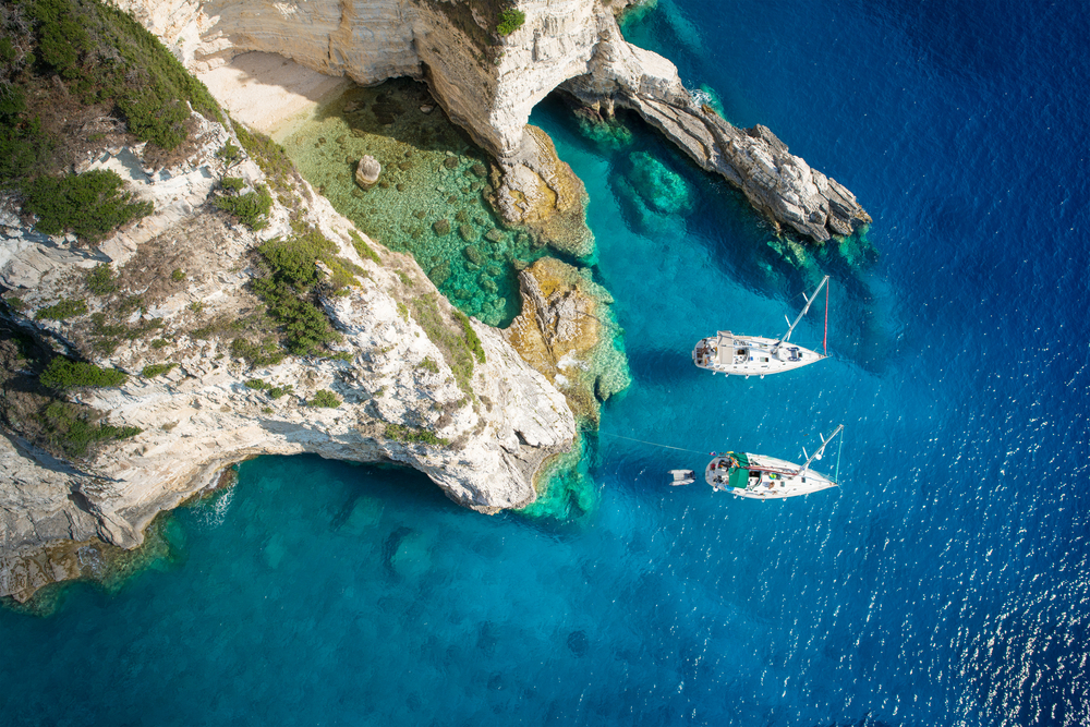 aerial photo of two boats in the water on the rocky coast of a white sandy beach with see-through water, clear water in Europe