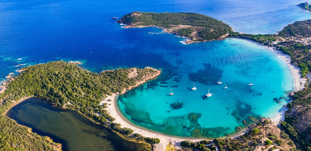 a circular bay in Europe with translucent water, there are boats in the bay and sandy beaches in the photo