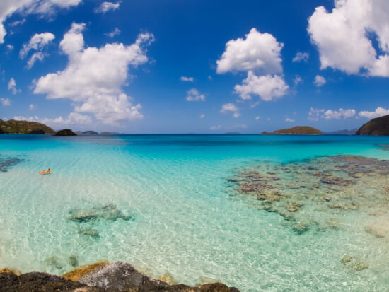 clear blue water of the USVI with rocks and clouds in a blue sky