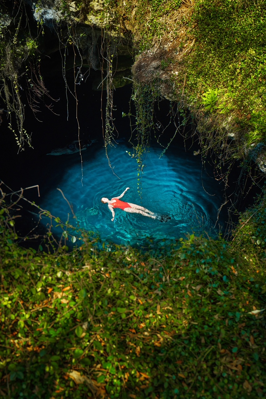 From the open hole in the floor- but technically the ceiling of Devil's Den- you can peer down and see a woman in a red suit floating in the clear water. 