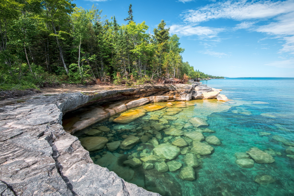 The coast of Lake Superior features bright green trees, rocky shorelines, and blue, clear waters.