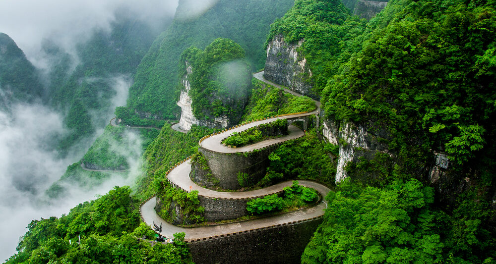 beautiful winding road with green trees and misty clouds