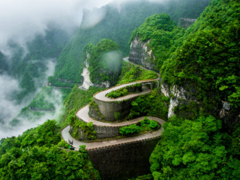 beautiful winding road with green trees and misty clouds