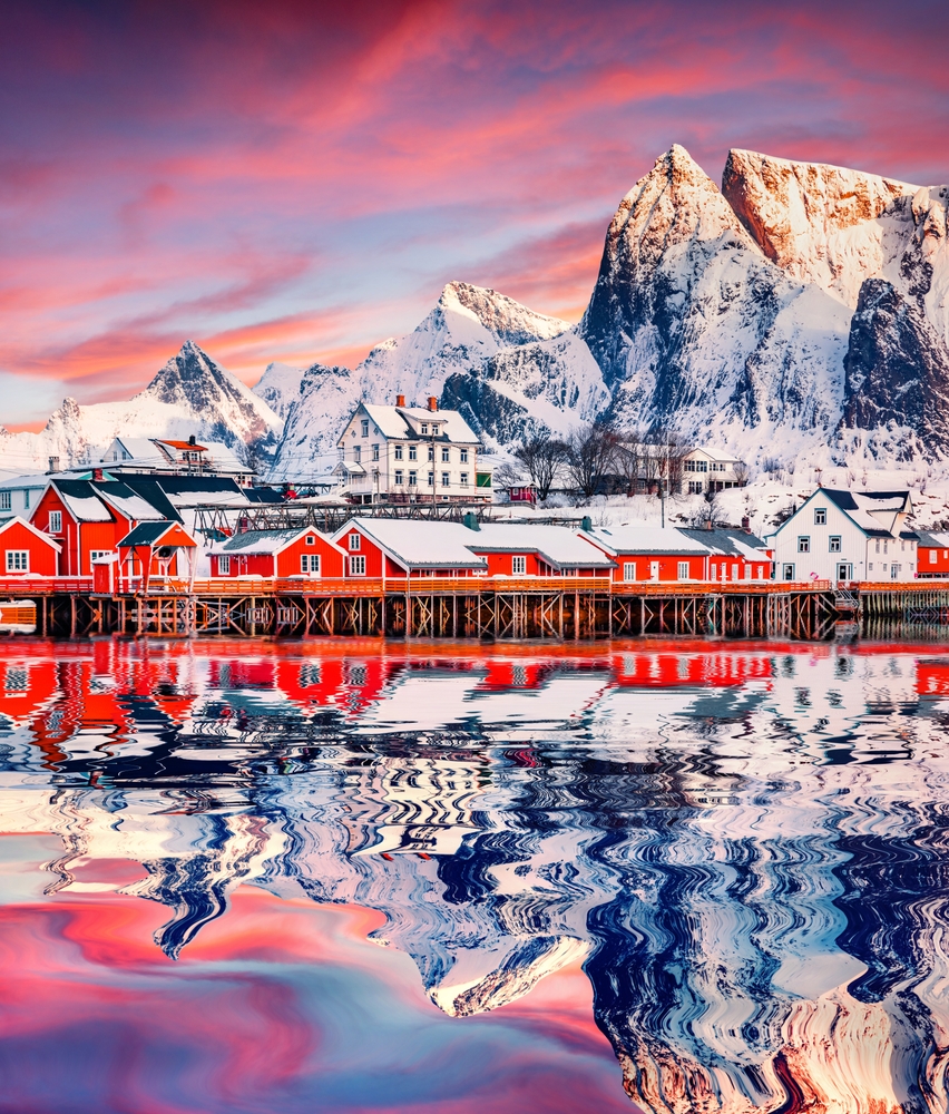 Red wooden houses reflected in calm waters of Gravdal bay. Great minter scene of popular tourist destination - Lofoten Islands. Beautiful seascape of Norwegian sea, Sakrisoy village, Norway, Europe