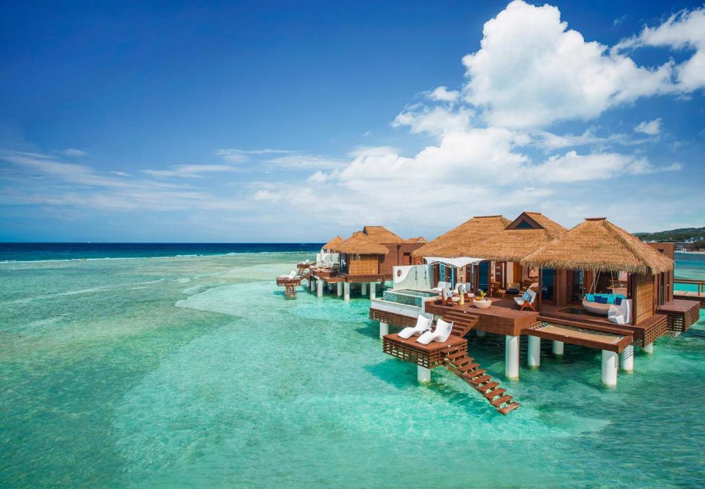 View of two overwater bungalows . You can see a pool a large deck with chairs and a swinging chair. 