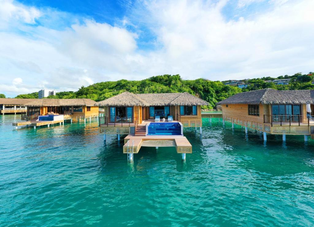 views from the sea of some water villas. you can see a plunge pool with a deck and chairs and the rooms with large windows. 