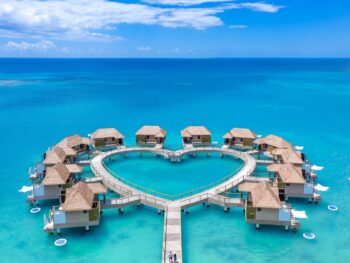 drone shot of heart shaped overwater bungalows with two people walking out to them over blue water