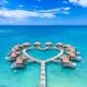 drone shot of heart shaped overwater bungalows with two people walking out to them over blue water
