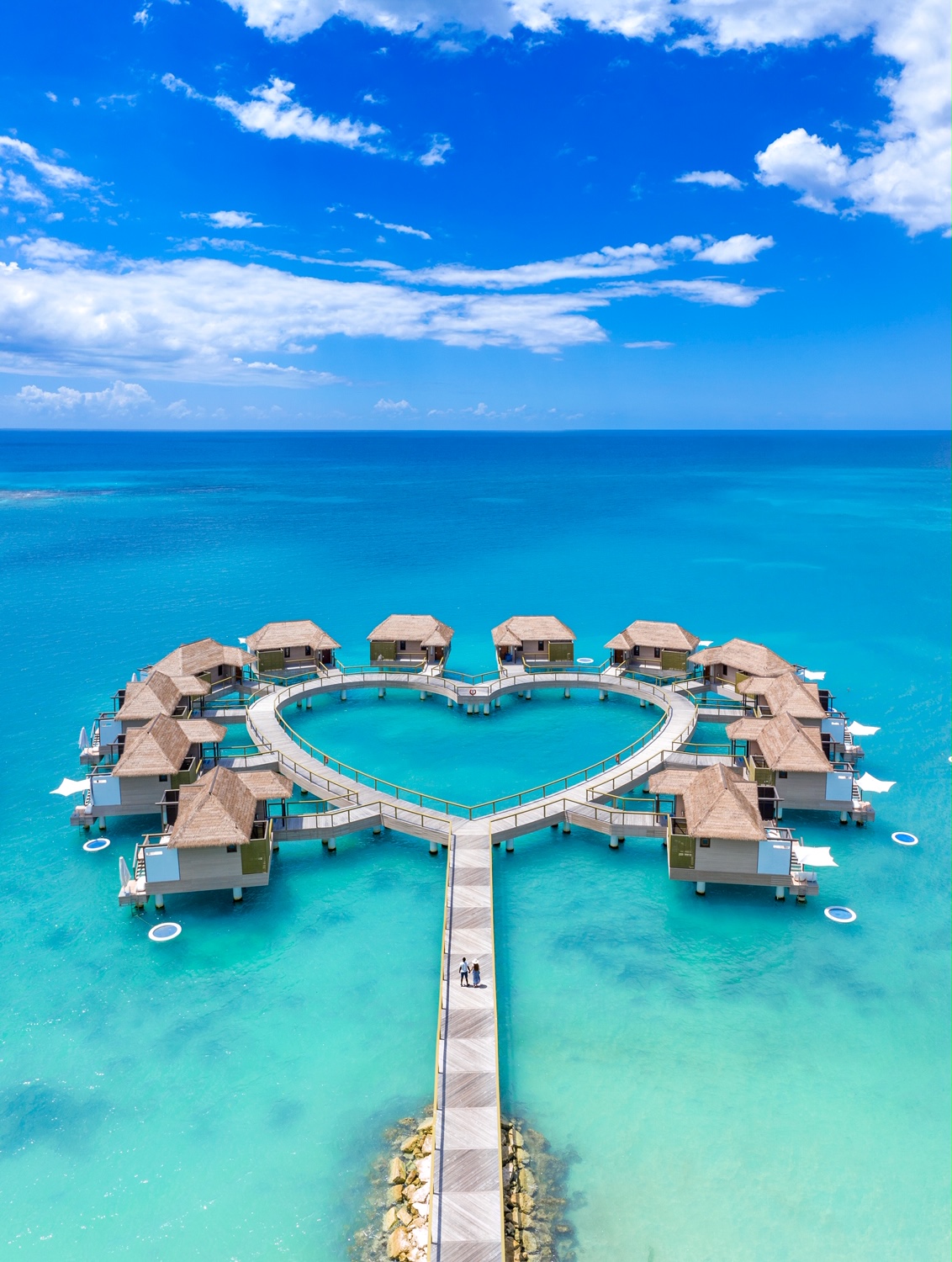 Couple walking over a wooden deck towards a ground of overwater bungalows near Florida that are around a heart shaped deck.  