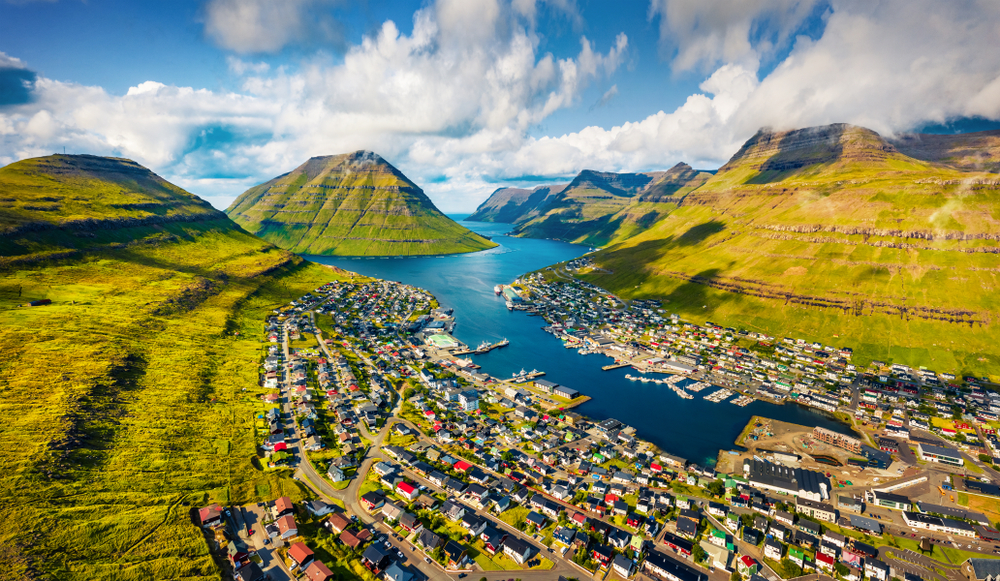 a fishing village in the Faroe islands, water I coming up between two mountains into the village, it is a partly cloudy day 