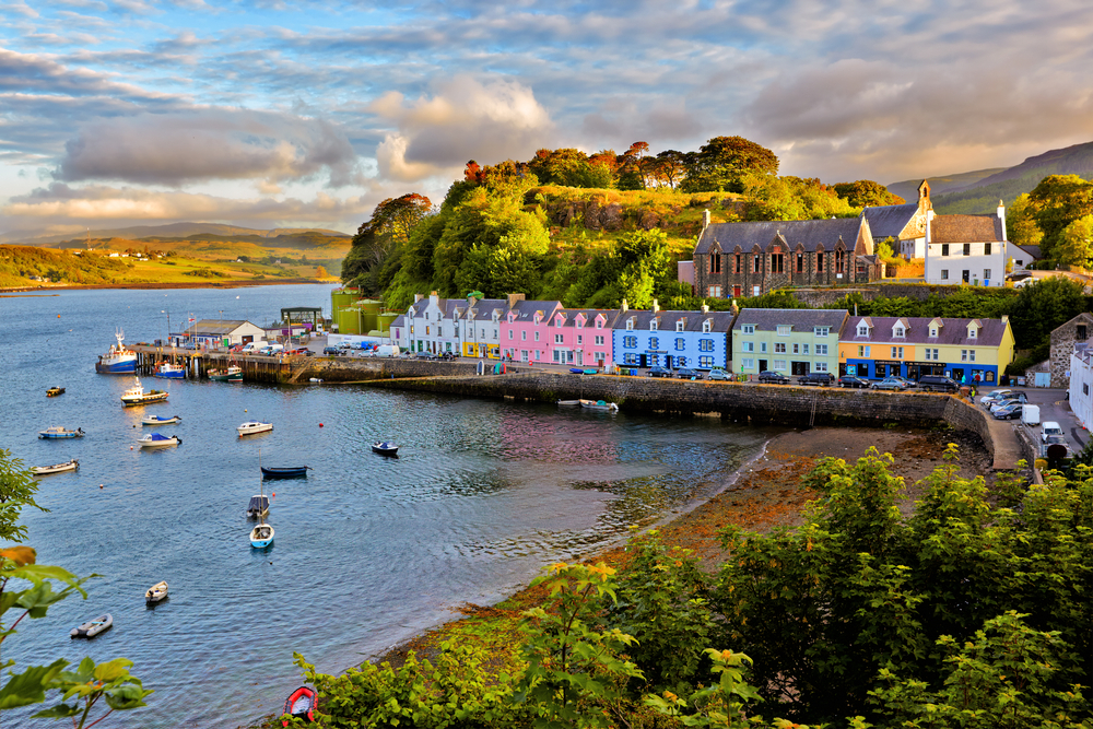 colorful houses on the waters edge in Scotland, one of the best places to visit in Europe in august, there are boats docked in the water in front of the colorful houses 