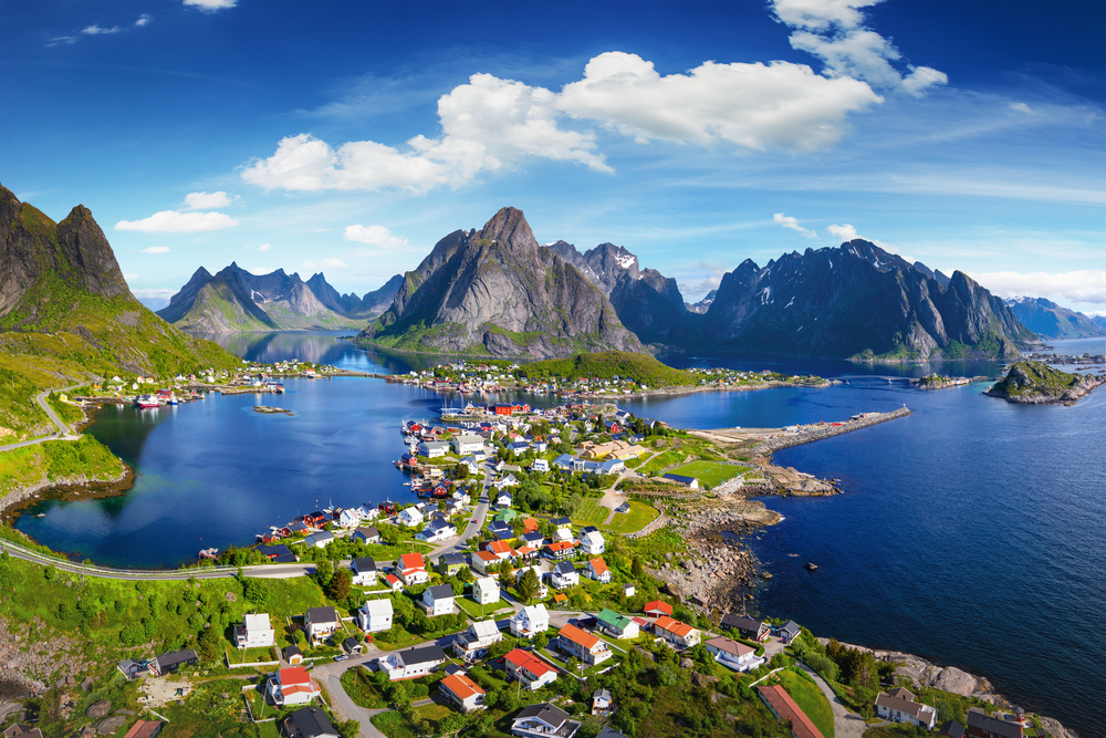 aerial photo of lofoten islands, a town is in the middle of the photo with water on three sides and mountains in the background