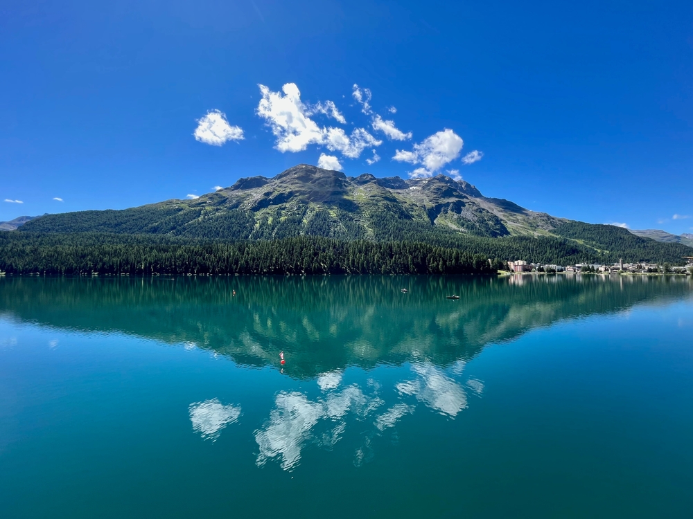 a mountain in the center of the photo with trees in front of it, in front of the trees and mountain is a lake in St. Mortiz Switzerland 