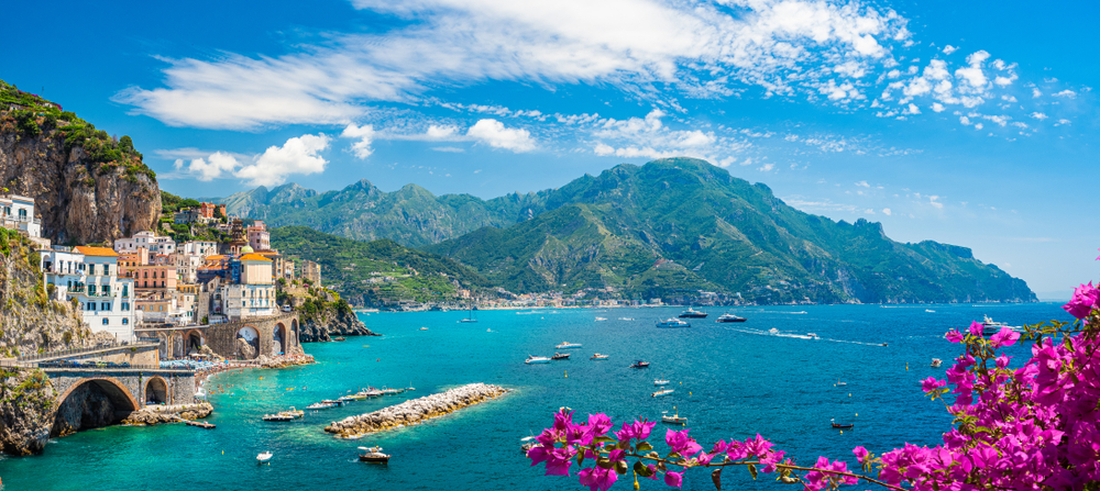 the town of Atrain on the Amalfi Coast cliffside town perched over the sea with mountains in the background and flowers in the foreground