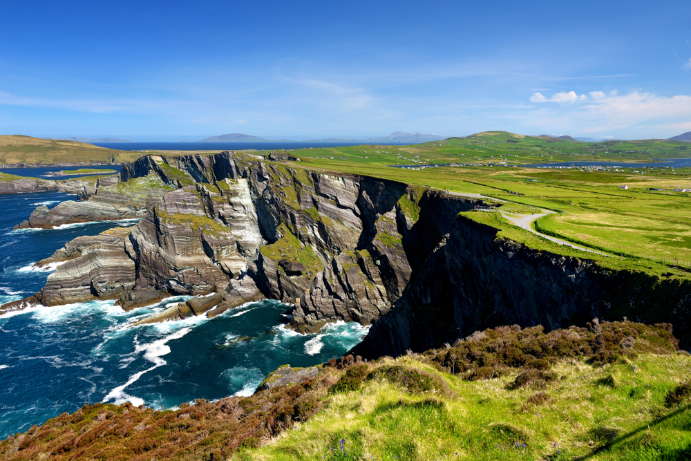 Rugged Kerry Cliffs with bright blue water below and green fields at the top.