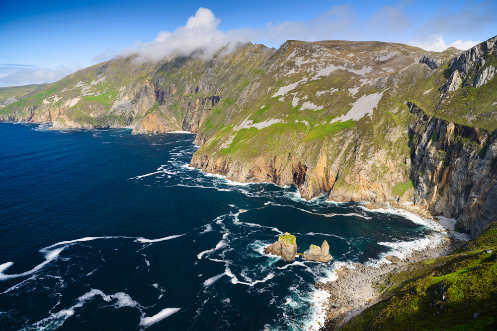 View looking down at the Slieve League Cliffs with blue water and rugged cliffs on a partly cloudy day.