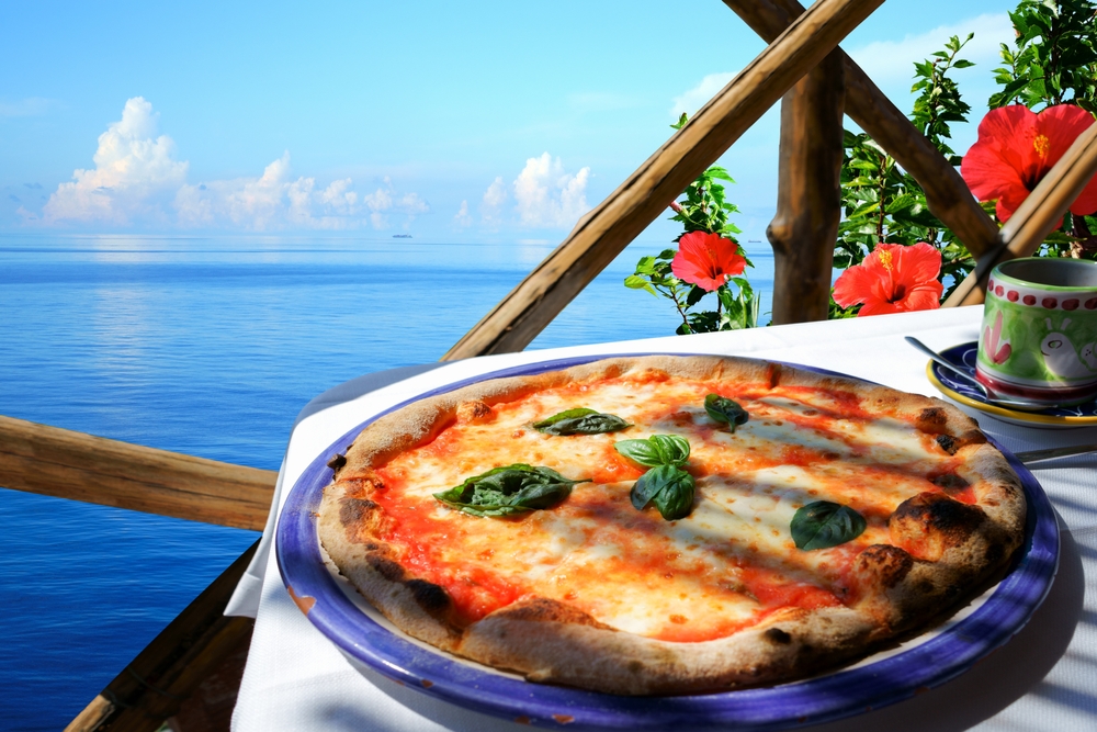 a table with a pizza overlooking the blue ocean