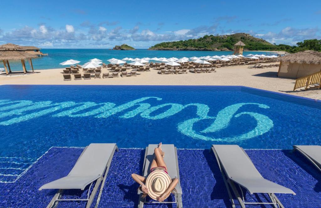 A woman lounging on a chaise in the a sparkling blue pool with the beach and the ocean in the background at Royalton Antingua, one of the best Marriott all inclusive resorts. 