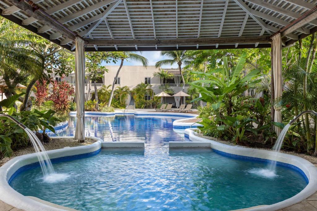 View from the spa with two spouts of water pouring into it to the pool. The water is surrounded by various trees, palms, and other plants. 